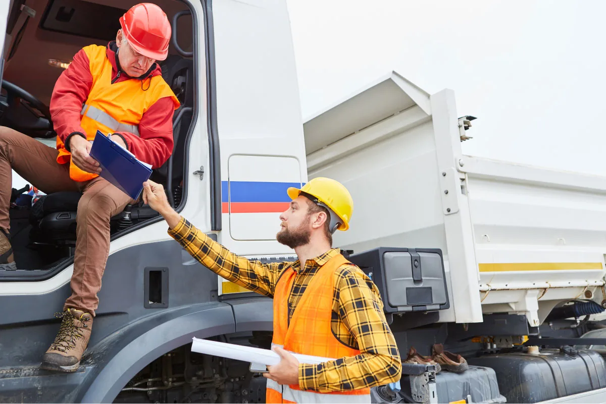 two men in hardhats talking, one standing and one sitting in a truck